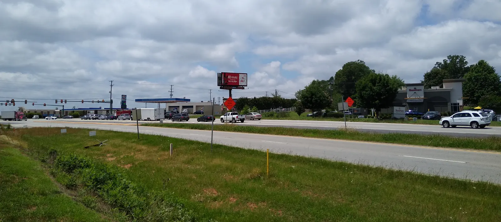 US Route 521 in Indian Land, South Carolina: a divided highway with a grassy median, orange road-work signs, a fuel station and a retail building under a cloudy sky